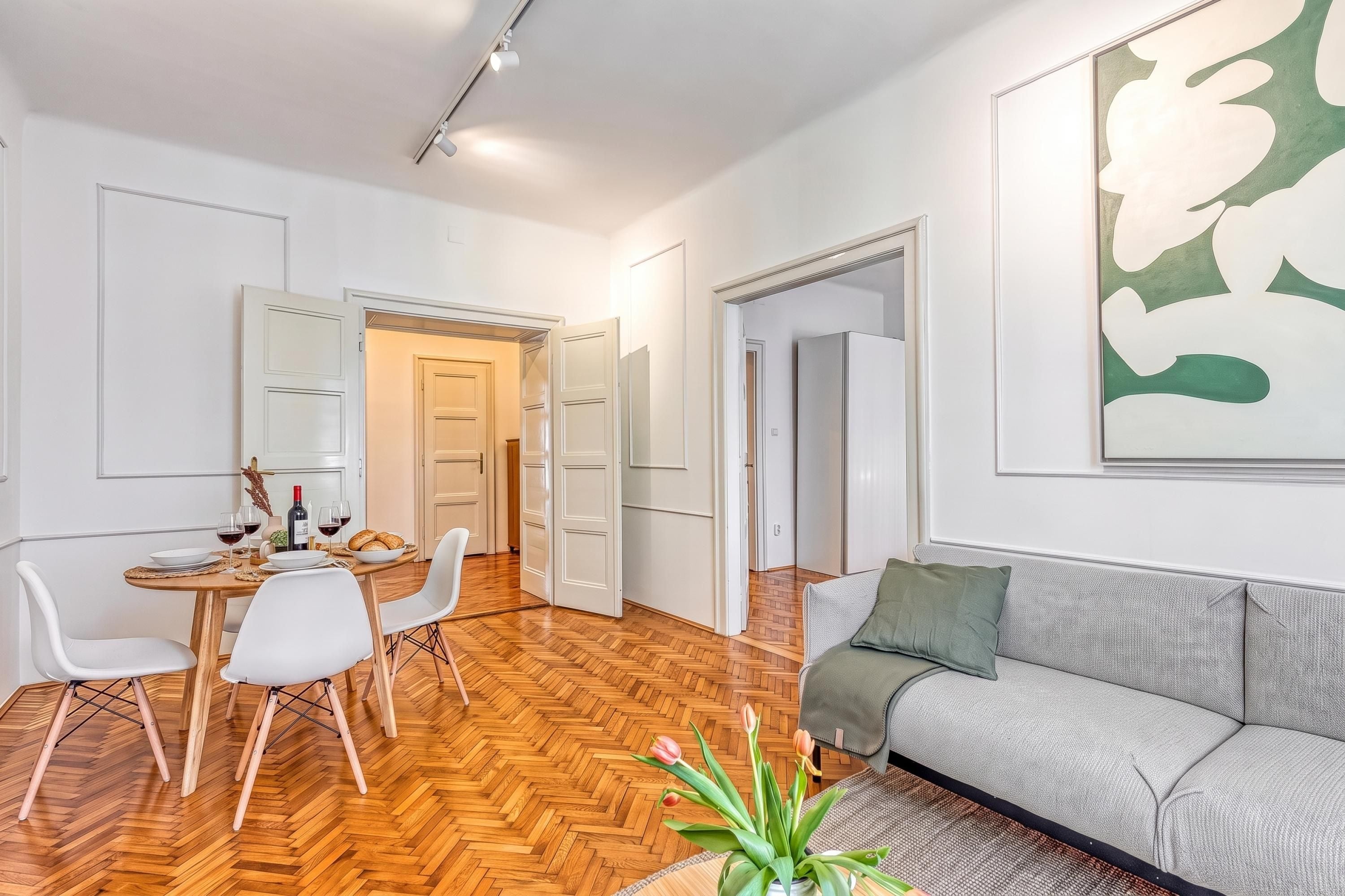 A modern living room with a sofa, dining table, chairs, and a large abstract painting on the wall.