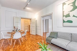 A modern living room with a sofa, dining table, chairs, and a large abstract painting on the wall. - Spacious Apartment In Heart Of Zagreb (Zagreb)