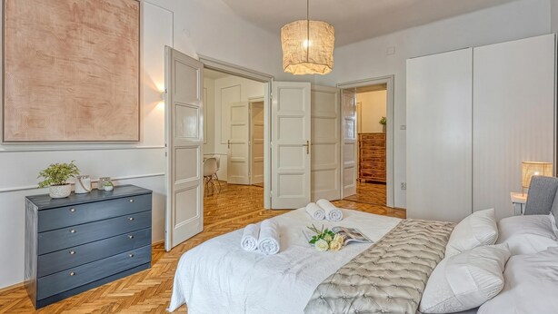 A bedroom with a bed, a dresser, a hanging light fixture, and a door leading to another room. - Spacious Apartment In Heart Of Zagreb (Zagreb)