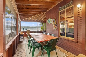 A covered outdoor dining area with a wooden table and chairs, a view of the lake, and a sign welcoming guests to Camp Run-A-Muk. - Camp Run-a-muk on Lake Waukewan (Meredith)