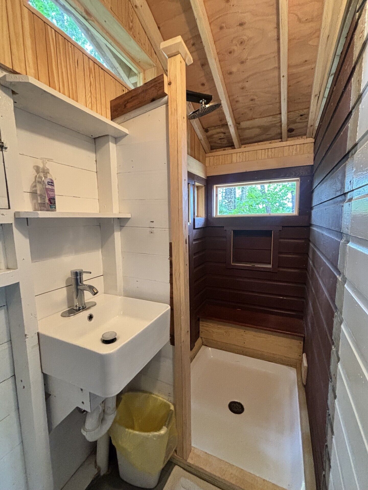 Une petite salle de bain avec un lavabo blanc, une fenêtre et un espace douche.