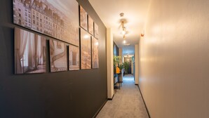A hallway with framed pictures on the wall, a carpeted floor, and a light fixture on the ceiling. - Woodbury 2-5 (Lancaster)