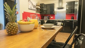A kitchen with a wooden table set for breakfast, including a pineapple, a bowl of fruit, and a glass of juice. - Woodbury 2-5 (Lancaster)