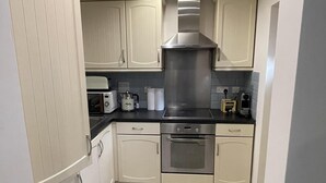 A compact kitchen with white cabinets, a stainless steel range hood, and a black countertop. - Lovely 1-bed Apartment in Town Centre Colchester (Colchester)