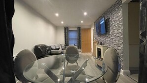 A modern living room with a glass dining table, leather sofa, and a stone accent wall. - Lovely 1-bed Apartment in Town Centre Colchester (Colchester)