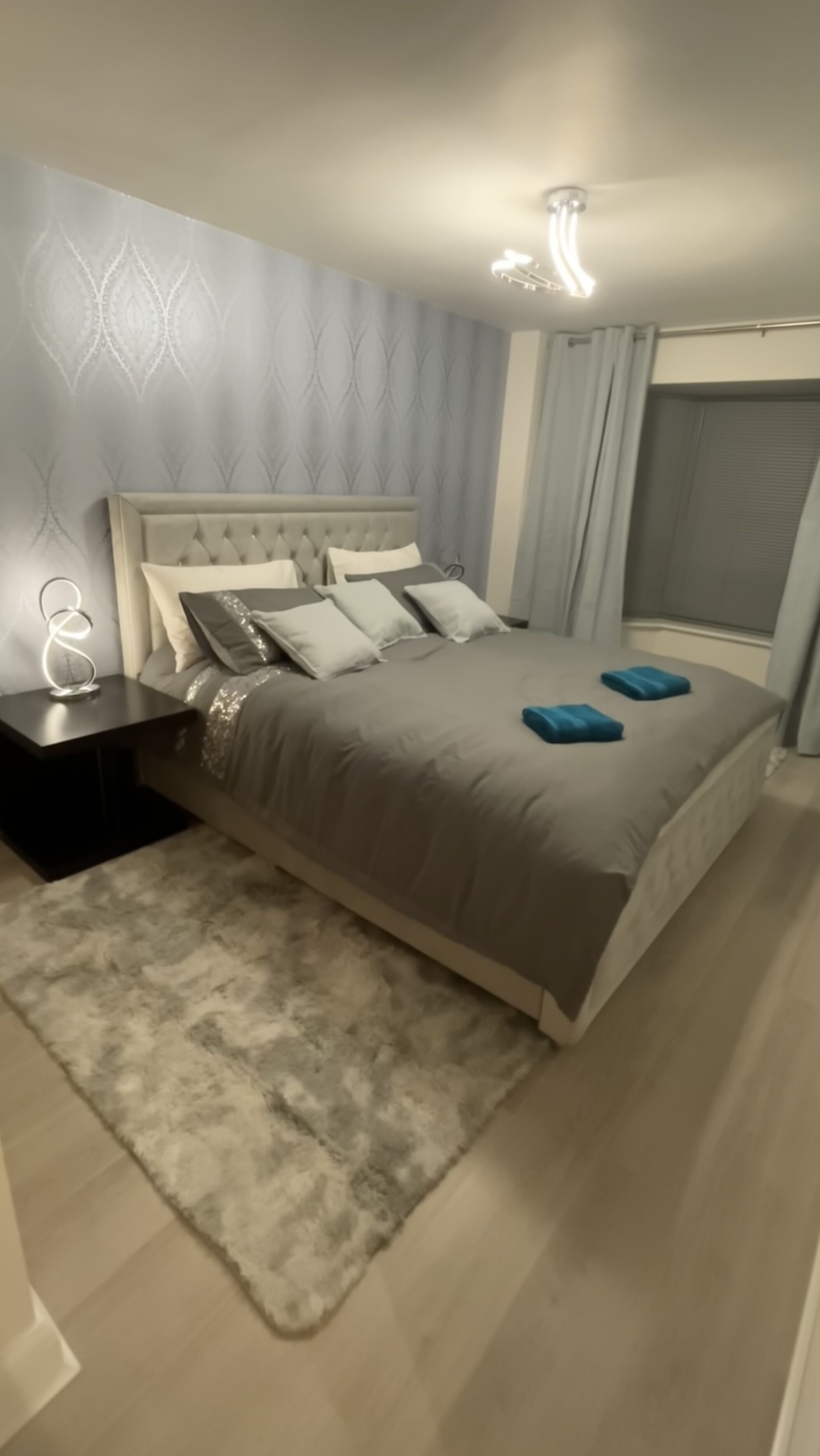 Ein modernes Schlafzimmer mit einem gesteppten Kopfteil, einer grauen Bettdecke und einem flauschigen Teppich.