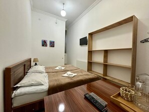 Una camera d'albergo con un letto, un comodino in legno, una televisione e una scaffalatura.