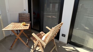 An outdoor patio with a wooden table and two chairs, a sliding glass door, and a window with blinds. - Loft33 (Barletta)