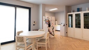 A dining area with a round table and four chairs, a kitchen with cabinets, and a large window. - Loft33 (Barletta)