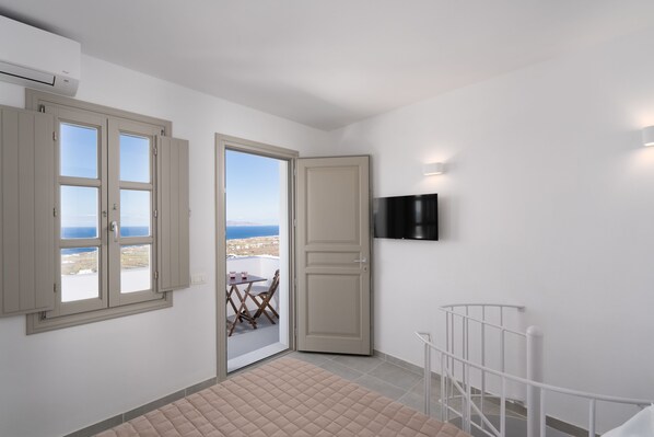 Una habitación con balcón, un televisor montado en la pared y una puerta que da al exterior.