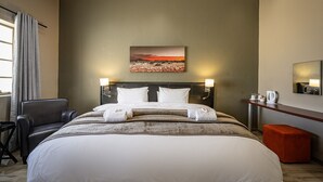 A hotel room with a large bed, two bedside tables, a chair, a desk, and a painting on the wall. - Pofadder Hotel (Pofadder)