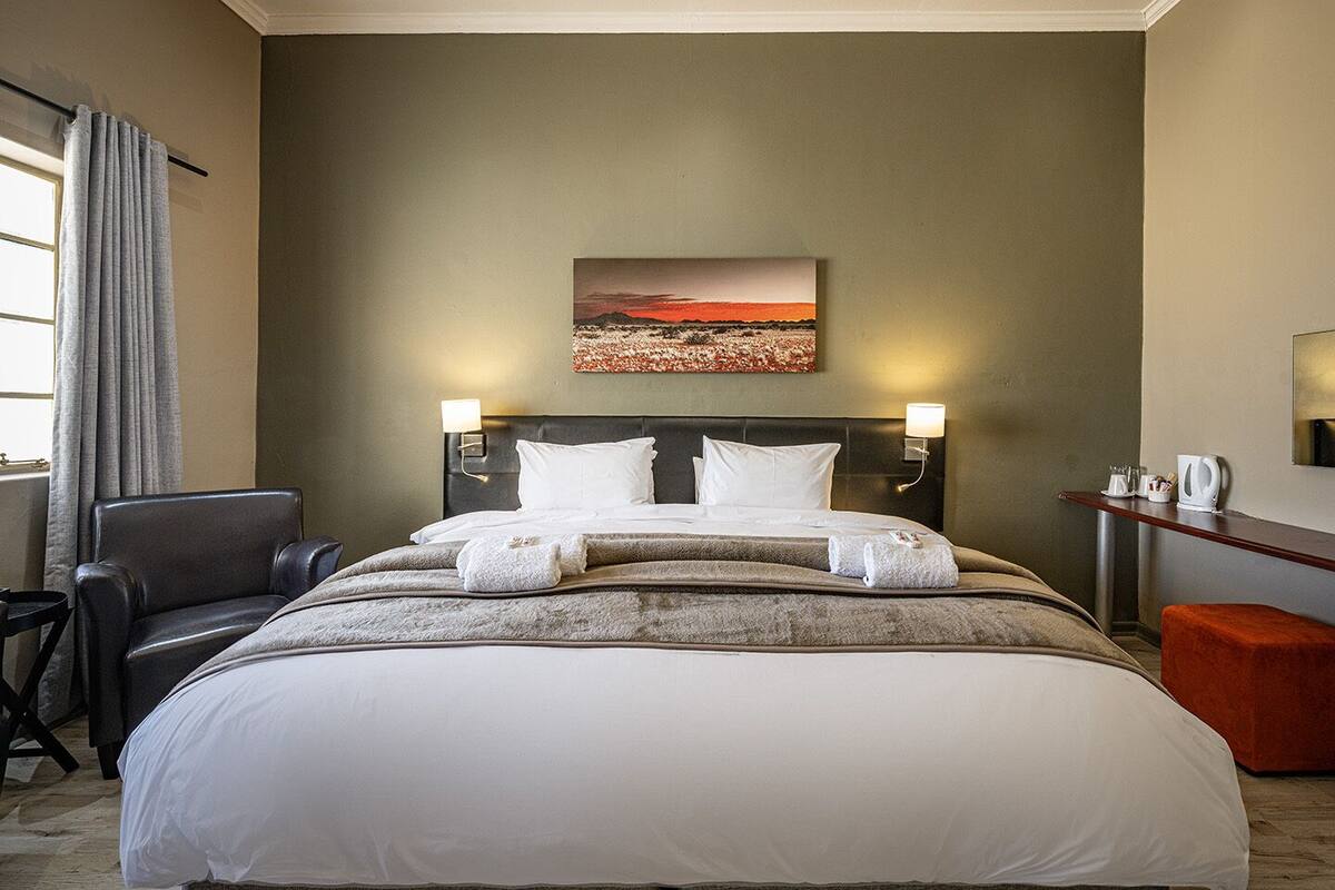 A hotel room with a large bed, two bedside tables, a chair, a desk, and a painting on the wall.