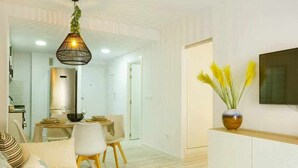 A modern living room with a dining area, a sofa, a TV mounted on the wall, and a decorative vase with yellow flowers. - Apartment Pink Arena (Torrevieja)