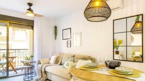 A modern living room with a sofa, coffee table, and dining table. There are ceiling fans, pendant lights, and a large window. - Apartment Pink Arena (Torrevieja)