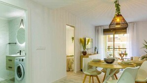 A modern kitchen with a built-in washing machine, a dining area with a wooden table and chairs, and a large window with curtains. - Apartment Pink Arena (Torrevieja)