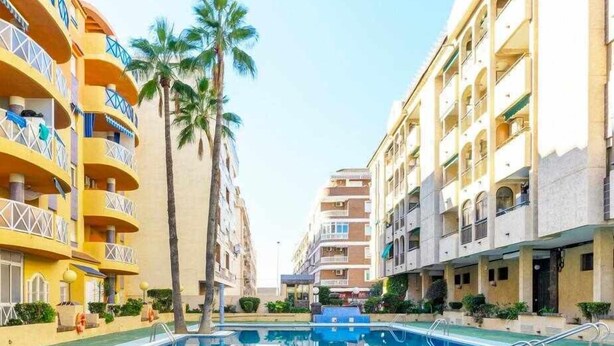 A hotel with a central swimming pool, multiple balconies, and palm trees. - Apartment Pink Arena (Torrevieja)