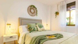 A bedroom with a bed, bedside table, and a window with curtains. - Apartment Pink Arena (Torrevieja)