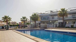 A swimming pool with a tiled deck, palm trees, and modern buildings in the background.