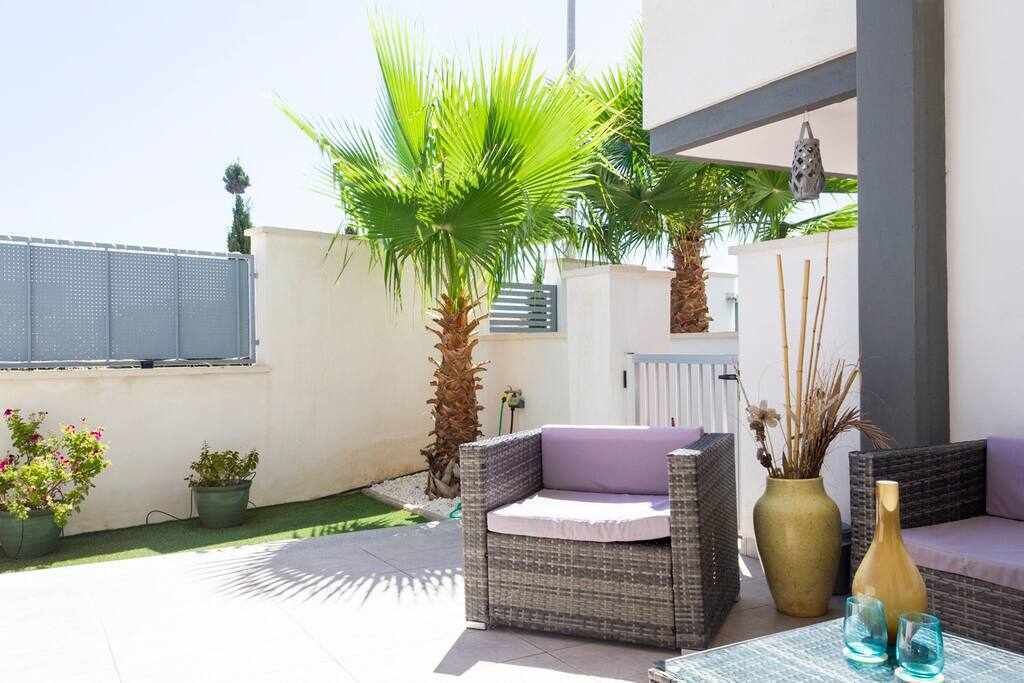 Un espace extérieur aménagé avec des meubles en osier, un palmier et des plantes en pot.