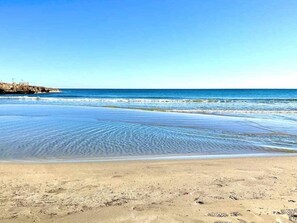 Una playa con agua cristalina, un promontorio rocoso y una orilla arenosa.