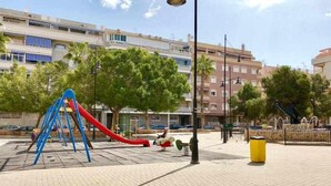 Une aire de jeux avec un toboggan rouge et une structure d’escalade bleue, entourée d’arbres et de bâtiments.