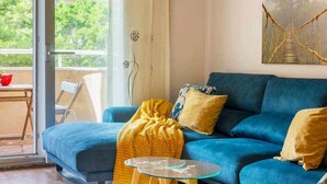 Un salon avec un canapé bleu, un plaid jaune et une table basse en verre.