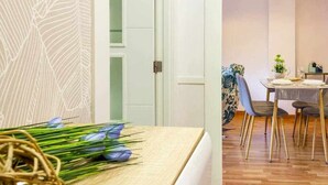 Une pièce comprenant un lit, un coin repas avec une table et des chaises, et un mur orné d’un motif de feuilles.