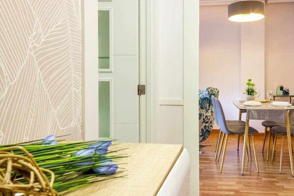 A room with a bed, a dining area with a table and chairs, and a wall with a leaf pattern.