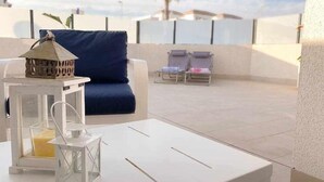 Eine Dachterrasse mit einem weißen Tisch, einem blauen Sofa und zwei Liegestühlen.