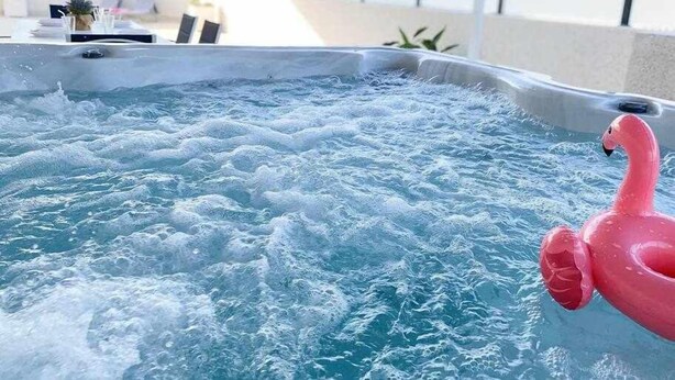 Ein Whirlpool mit einem rosa Flamingo-Schwimmpflege, umgeben von einem Poolbereich mit Liegestühlen und einem Tisch mit einer Pflanze.