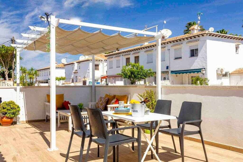 Eine Terrasse im Freien mit Tisch und Stühlen, einer Pergola und Blick auf Gebäude im Hintergrund.
