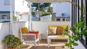 Ein Balkon mit einer weißen Bank und einem Tisch, umgeben von weißen Wänden und einem Blumentopf.