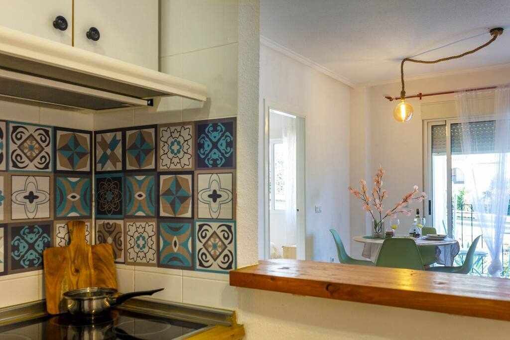 A kitchen with patterned tiles, a wooden countertop, and a view of a dining area with a table and chairs.