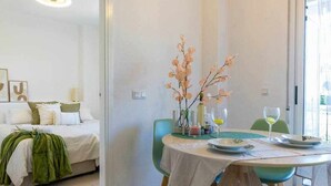 A room with a bed, a dining table with chairs, and a vase with flowers.