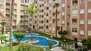 A multi-story hotel with balconies, a central swimming pool, and surrounding greenery. - Pink port apartment (Torrevieja)