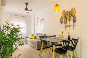 A modern living room with a sofa, dining table, chairs, and a ceiling fan. - Pink port apartment (Torrevieja)