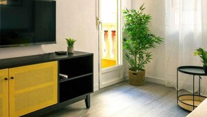 A living room with a flat-screen TV on a black and yellow cabinet, a potted plant, and a wicker basket on the floor. - Pink port apartment (Torrevieja)