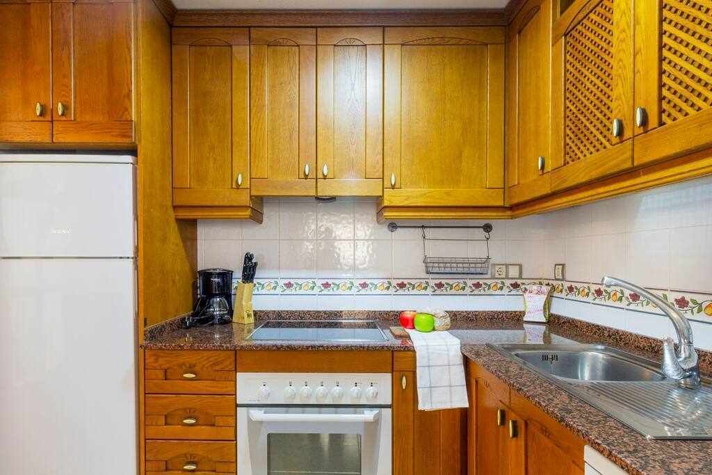 Una cocina con armarios de madera, un refrigerador blanco, estufa, lavaplatos y cafetera.