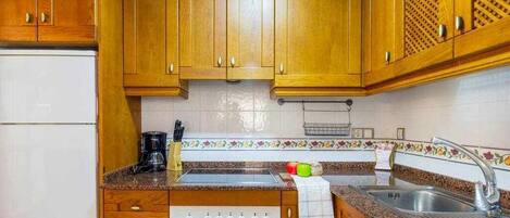 Una cocina con armarios de madera, un refrigerador blanco, estufa, lavaplatos y cafetera.