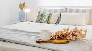Ein ordentlich gemachtes Bett mit weißer Daunendecke, einer weißen Tasse und einem Holftablett mit dekorativen Blättern.
