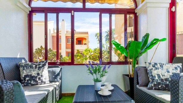 A balcony with wicker furniture, a potted plant, and a table with cups and saucers. - Lovely Groundfloor with swimming pool (Torrevieja)