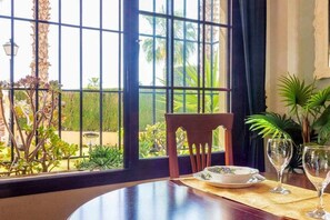 A dining table with a chair, a plate, and two wine glasses, set against a window with a view of a garden.