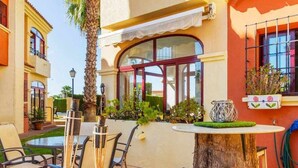 An outdoor patio with tables and chairs, a palm tree, and a window with a view of the street. - Lovely Groundfloor with swimming pool (Torrevieja)