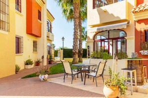 A courtyard with outdoor seating, a palm tree, and a building with a red and yellow facade.