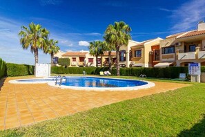 A residential complex with a swimming pool, palm trees, and a well-maintained lawn.
