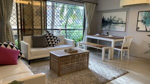 Una sala moderna con un sofá blanco, una mesa de centro de madera y un comedor con una mesa y sillas blancas.
