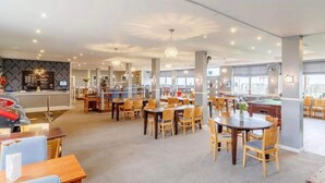 Un amplio vestíbulo de hotel con varias zonas de restauración, mesa de billar y una recepción.