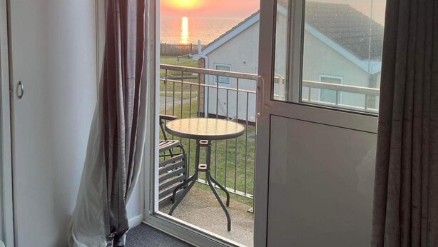 Un balcón con mesa y sillas, con vista a la puesta de sol sobre el mar.