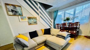 Una sala de estar con un sofá seccional, una mesa de comedor con sillas y una escalera con barandal a rayas.