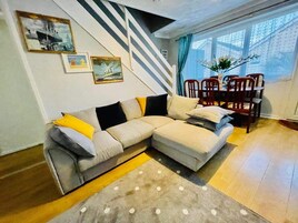 Una sala de estar con un sofá seccional, una mesa de comedor con sillas y una escalera con barandal a rayas.